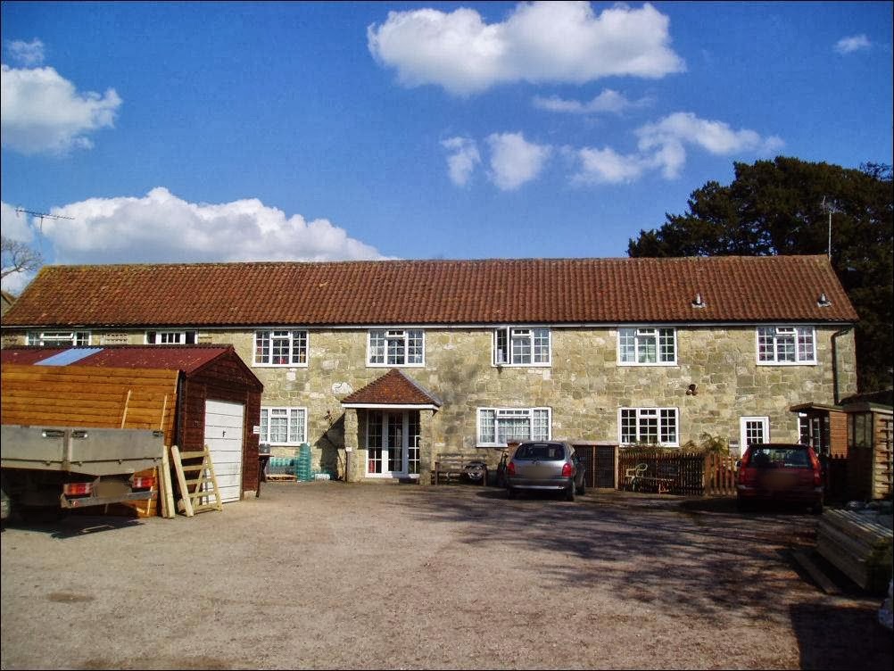 The Rope House: a long stone building with a red-tile roof, with a timber shed and garage, timber stacks and a trailer in front